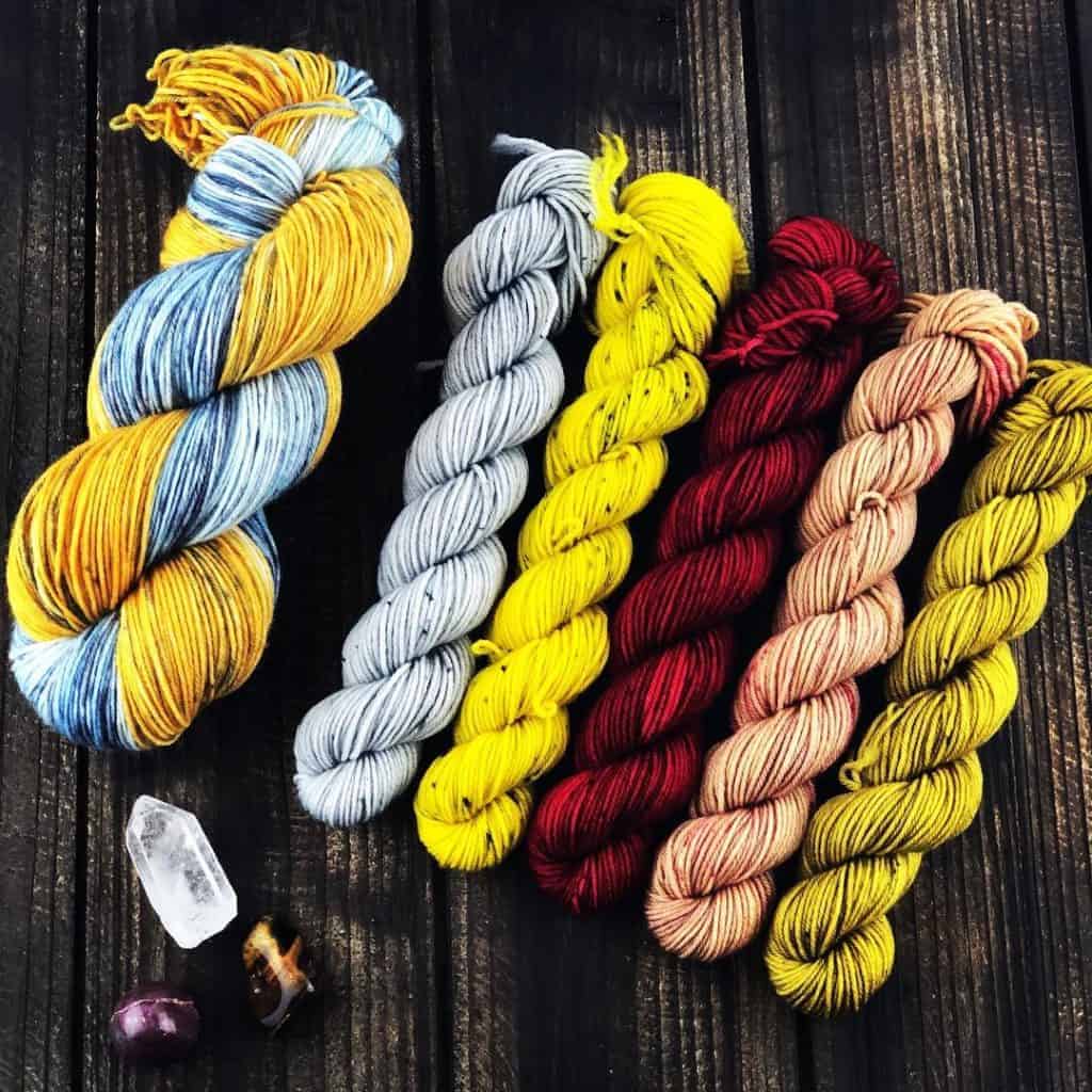 A set of grey, yellow, red, pink and gold mini skeins of yarn.