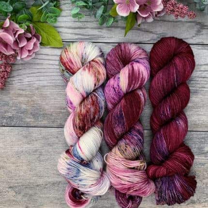 A set of three skeins of burgundy and pink yarn.