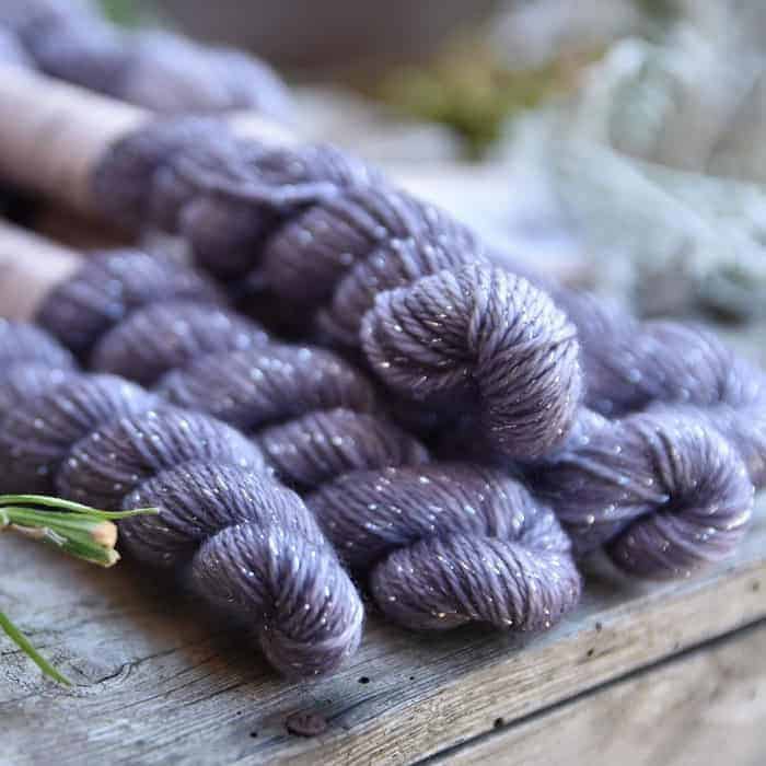 A set of five skeins of purple yarn with sparkles.