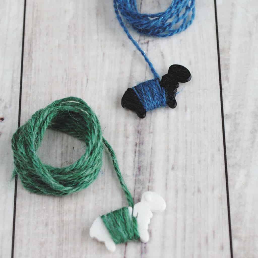 Tiny black and white sheep holding blue and green yarn.