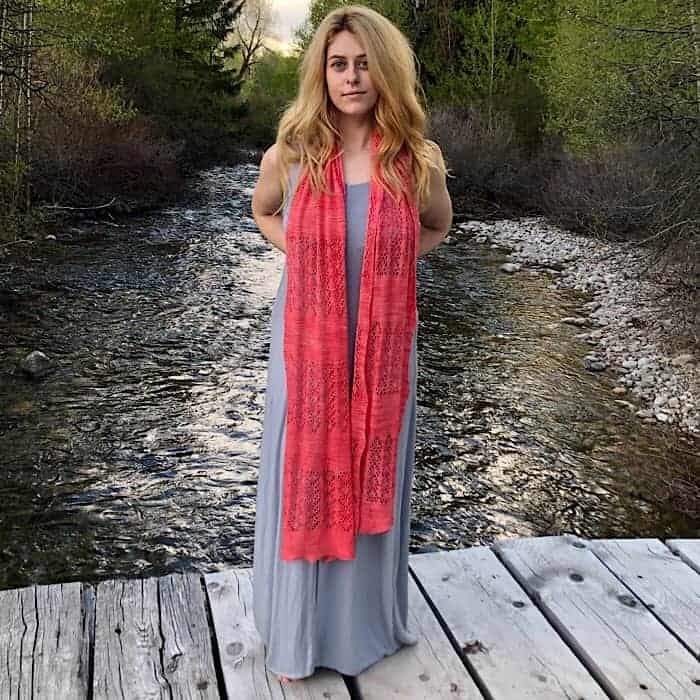 A model in a long gray dress wears a coral lace scarf.