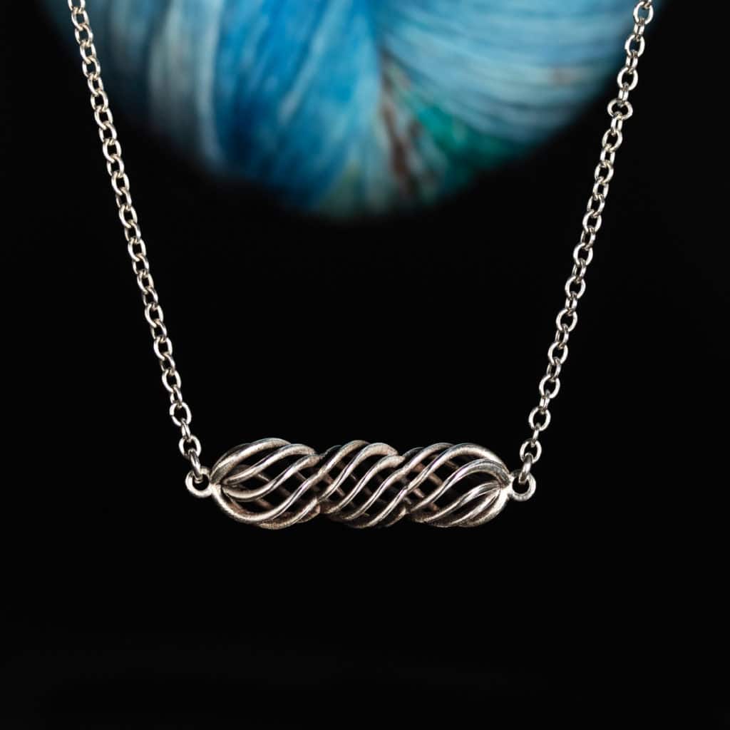 A silver twisted necklace in front of blue yarn.