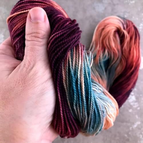 A hand squishes red, white and blue variegated yarn.