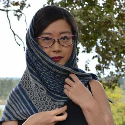 A woman models a blue and gray striped and lace shawl.