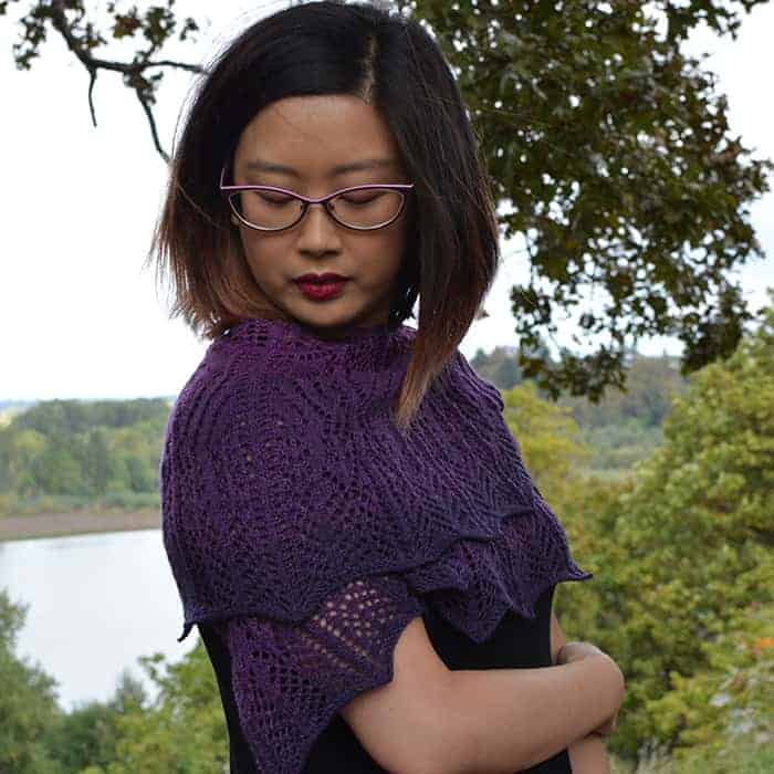 A knitter models a purple shawl