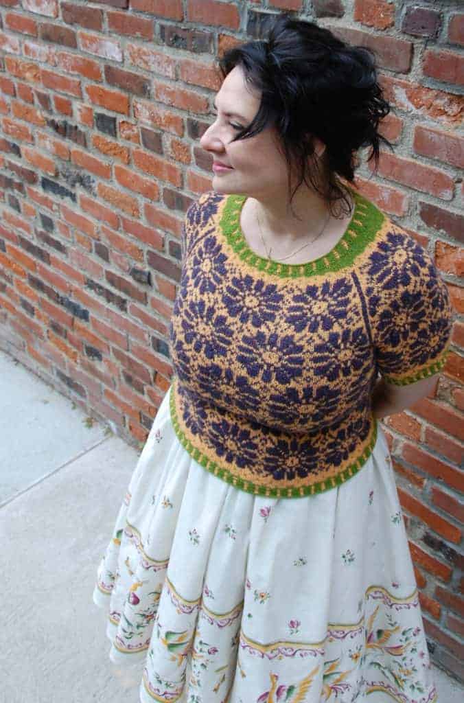 An orange sweater with a purple daisy pattern and a green accent at the neckline.