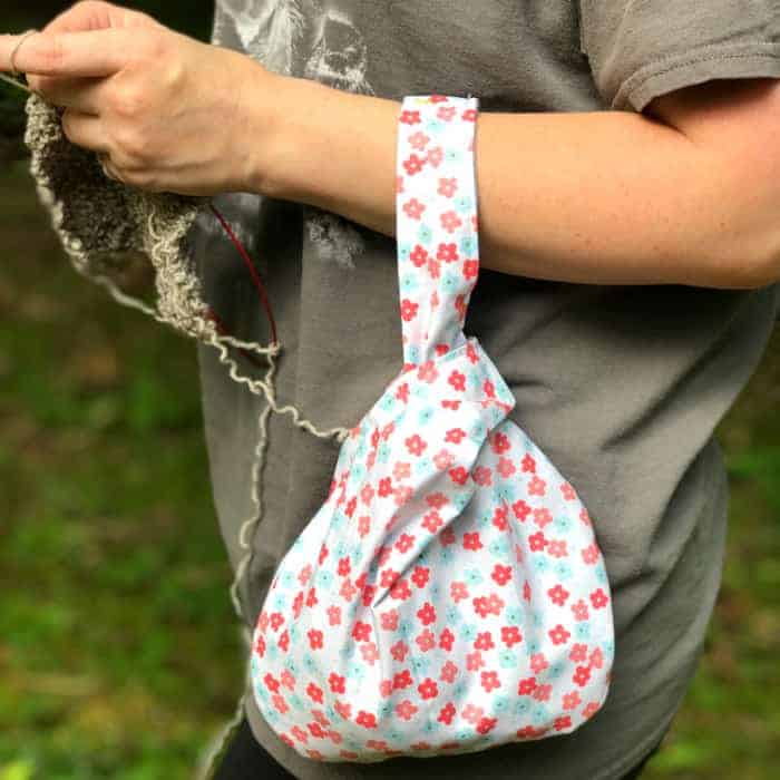 A project bag slung over a knitter's arm