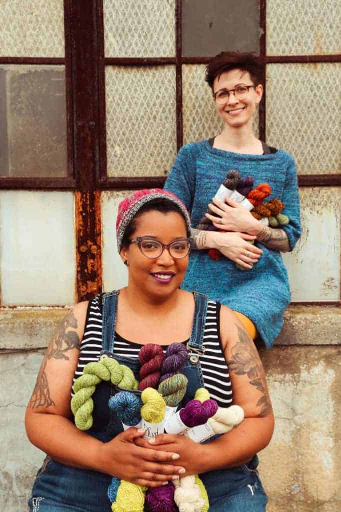 Two women hold skeins of colorful yarn.