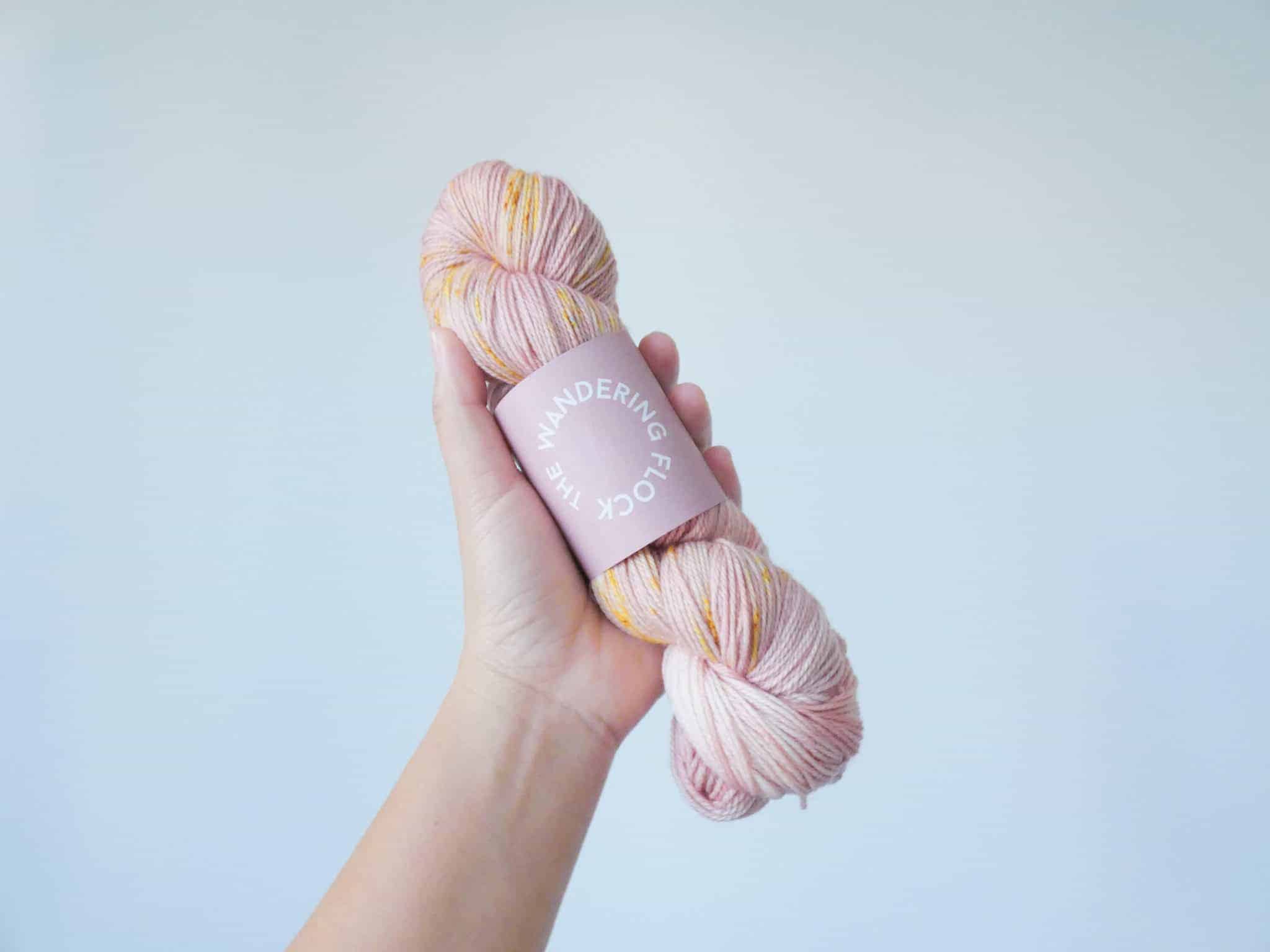 A hand holds a skein of rose gold yarn.