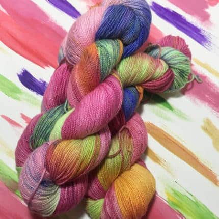 Skeins of pink, purple, green and orange yarn in front of a painting with the same colors.