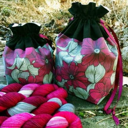 A pink and white floral bag with pink and white yarn.