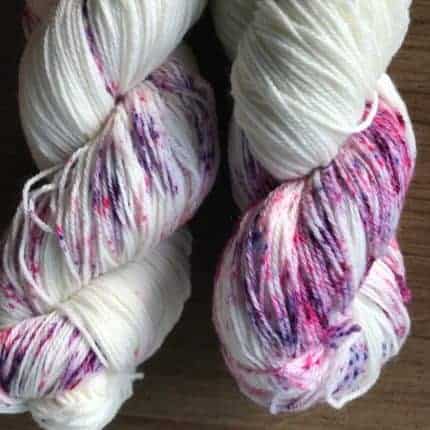 A skein of white yarn with pink and purple speckles.