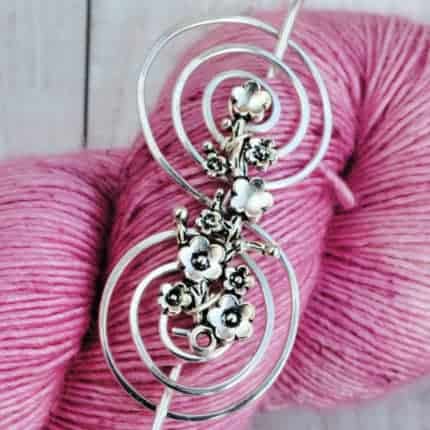 A silver shawl pin on a skein of pink yarn.