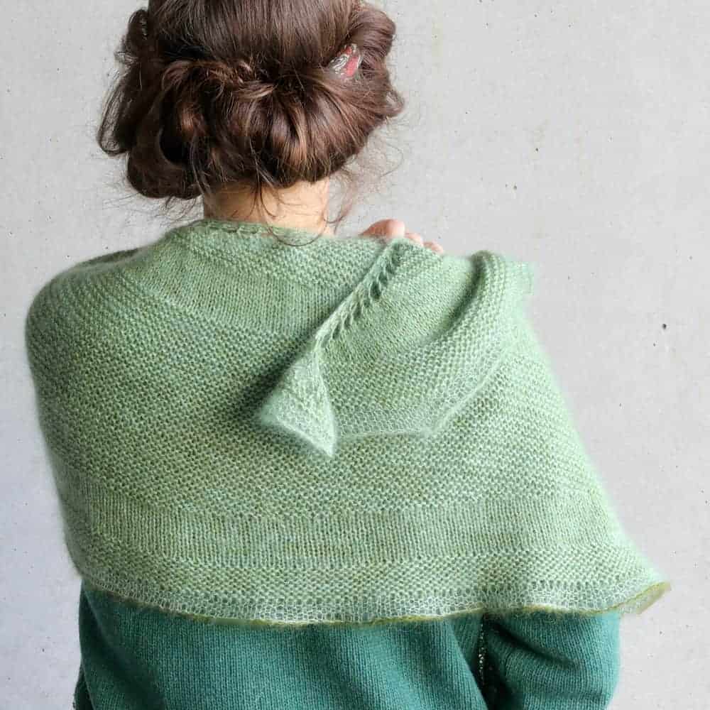 A mint green knit shawl sits on a woman's shoulders.