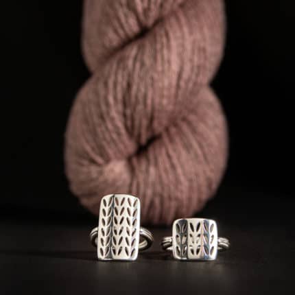 Silver rings sit in front of a skein of pink yarn.