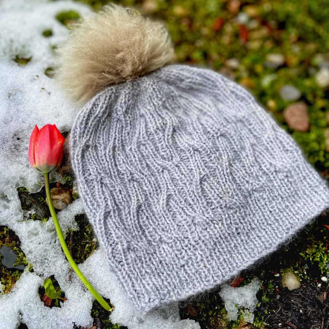 A silver cabled hat with a gold pompom.