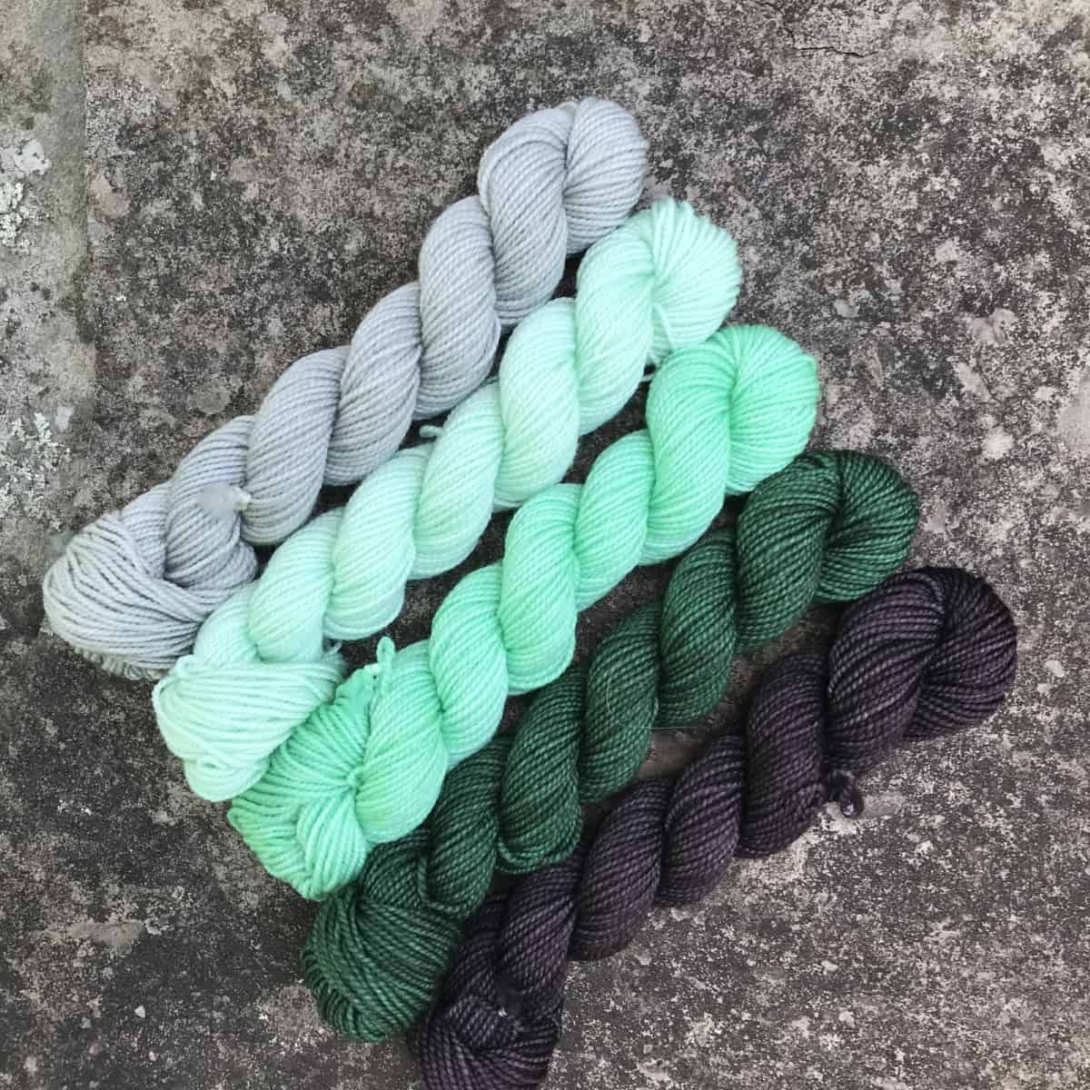 A set of gray to green mini skeins of yarn.