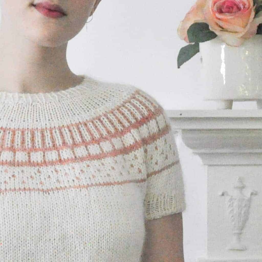 A woman models a white sweater with pale orange colorwork.