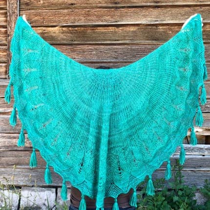 A teal shawl with lace and tassels.