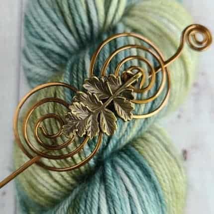 A bronze shawl pin with leaves on green yarn.