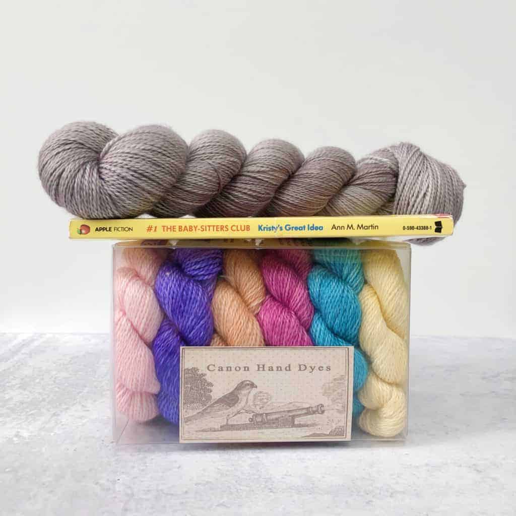 Gray yarn atop a book and a box of colorful mini skeins.