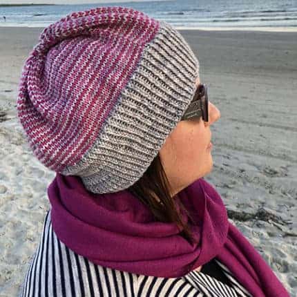 A woman models a purple and gray hat on a beach.