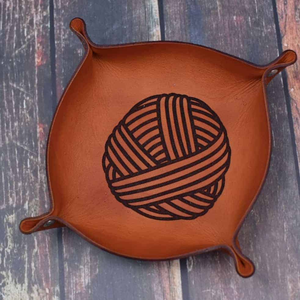 A leather tray with the image of a yarn ball. 