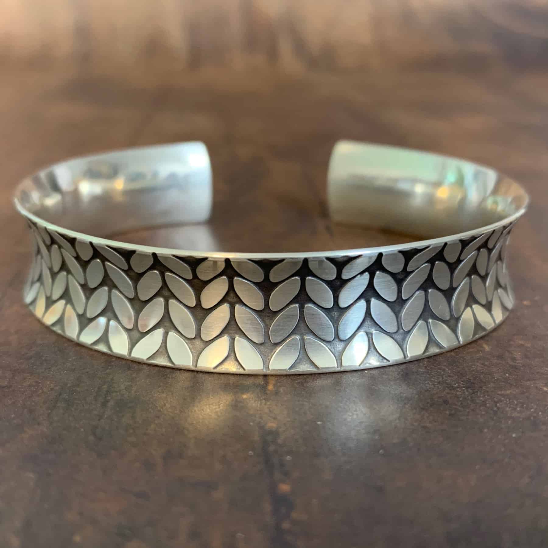 A silver bracelet with stockinette stitches etched into it. 