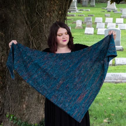A woman holds up a large blue triangular shawl.