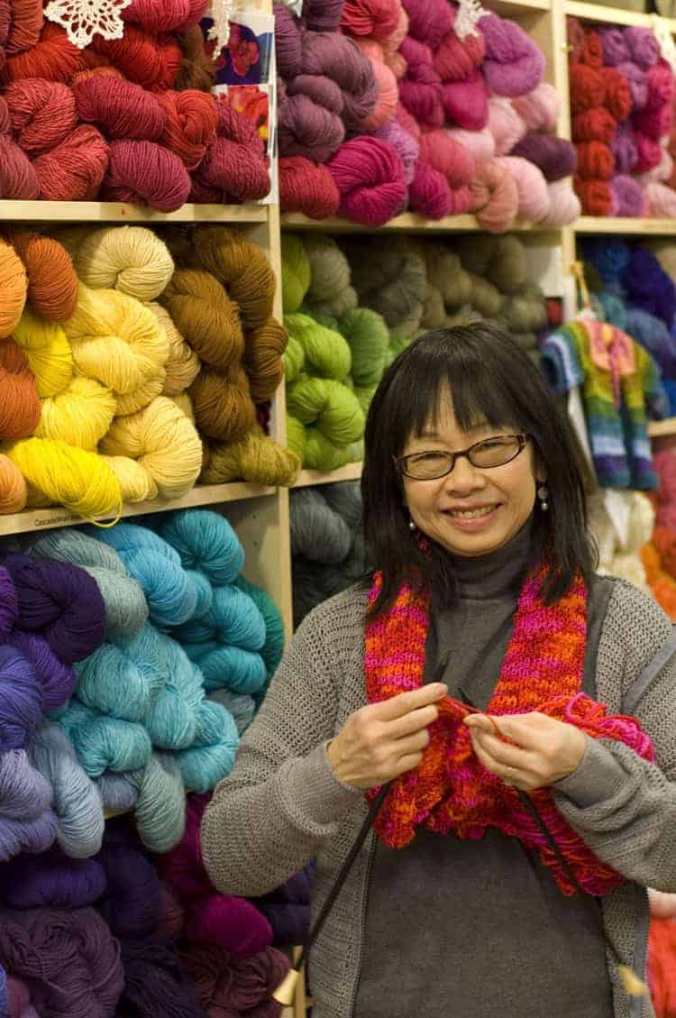 A woman stands in front of colorful yarn.