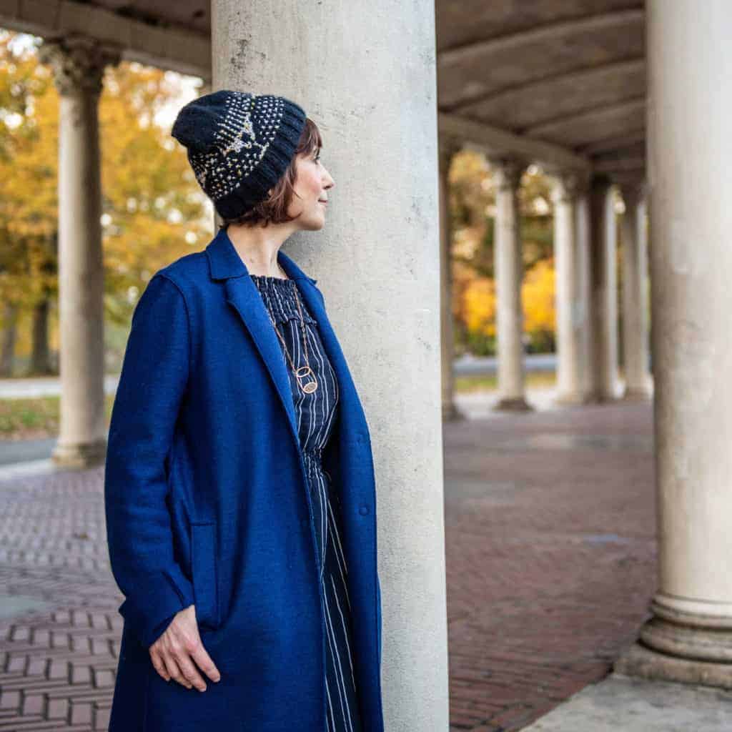 A woman models a blue and gray beanie next to columns.