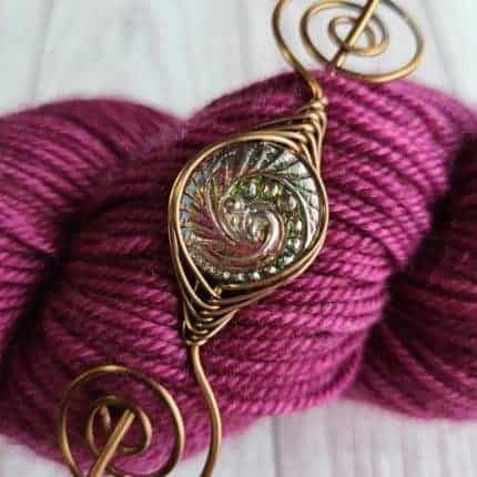 A bronze shawl pin on pink yarn.