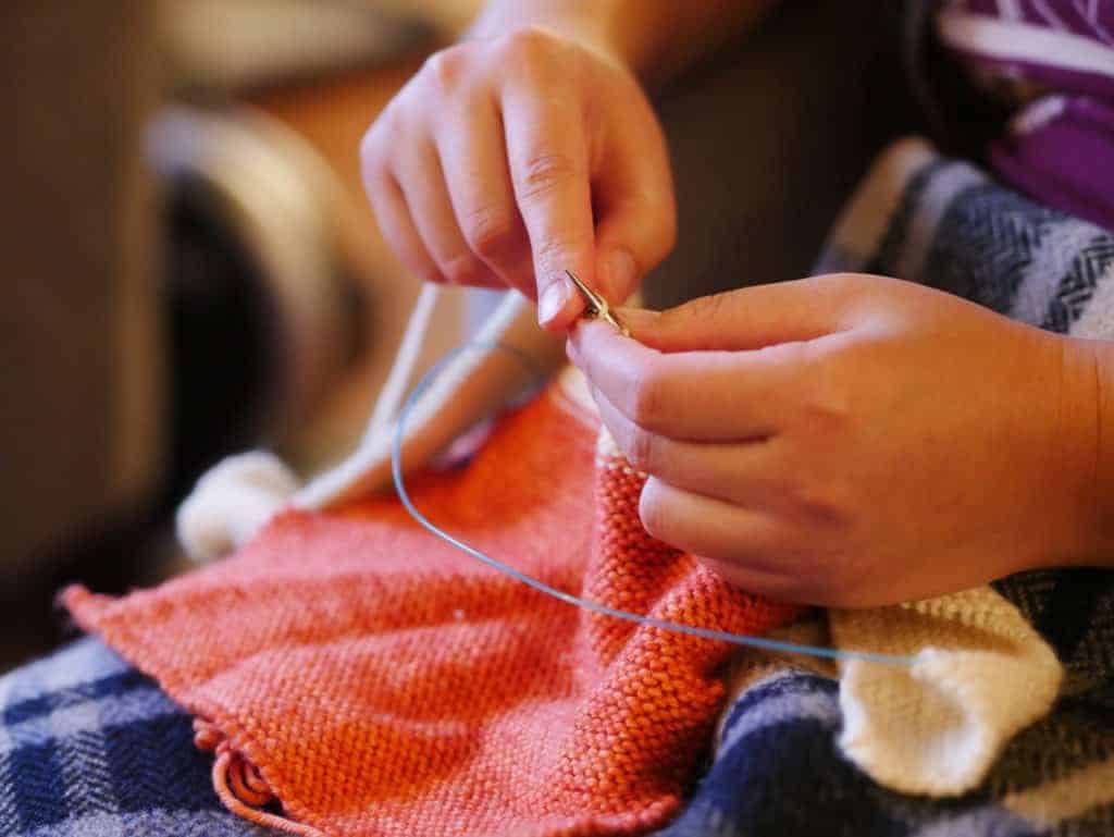 Hands knitting a coral sweater.