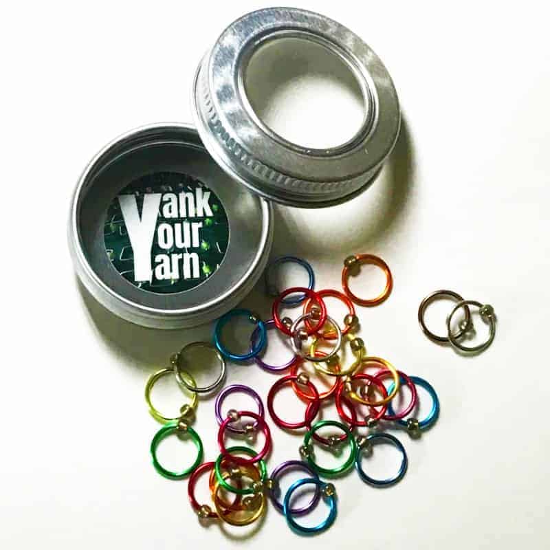 Colorful round metal loops next to a silver tin labeled with the words Yank Your Yarn.
