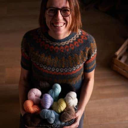 A smiling woman holds a basket of colorful yarn.