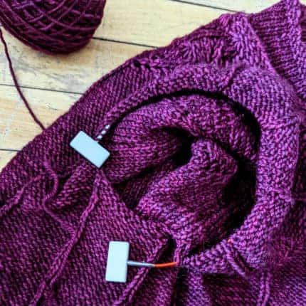 A purple knitting project on a red cord with white stoppers at the ends.