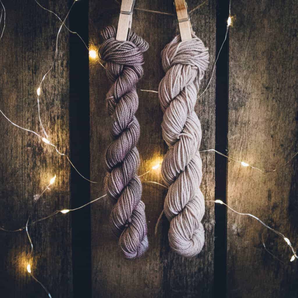 Skeins of gray yarn hanging on wooden clothespins.