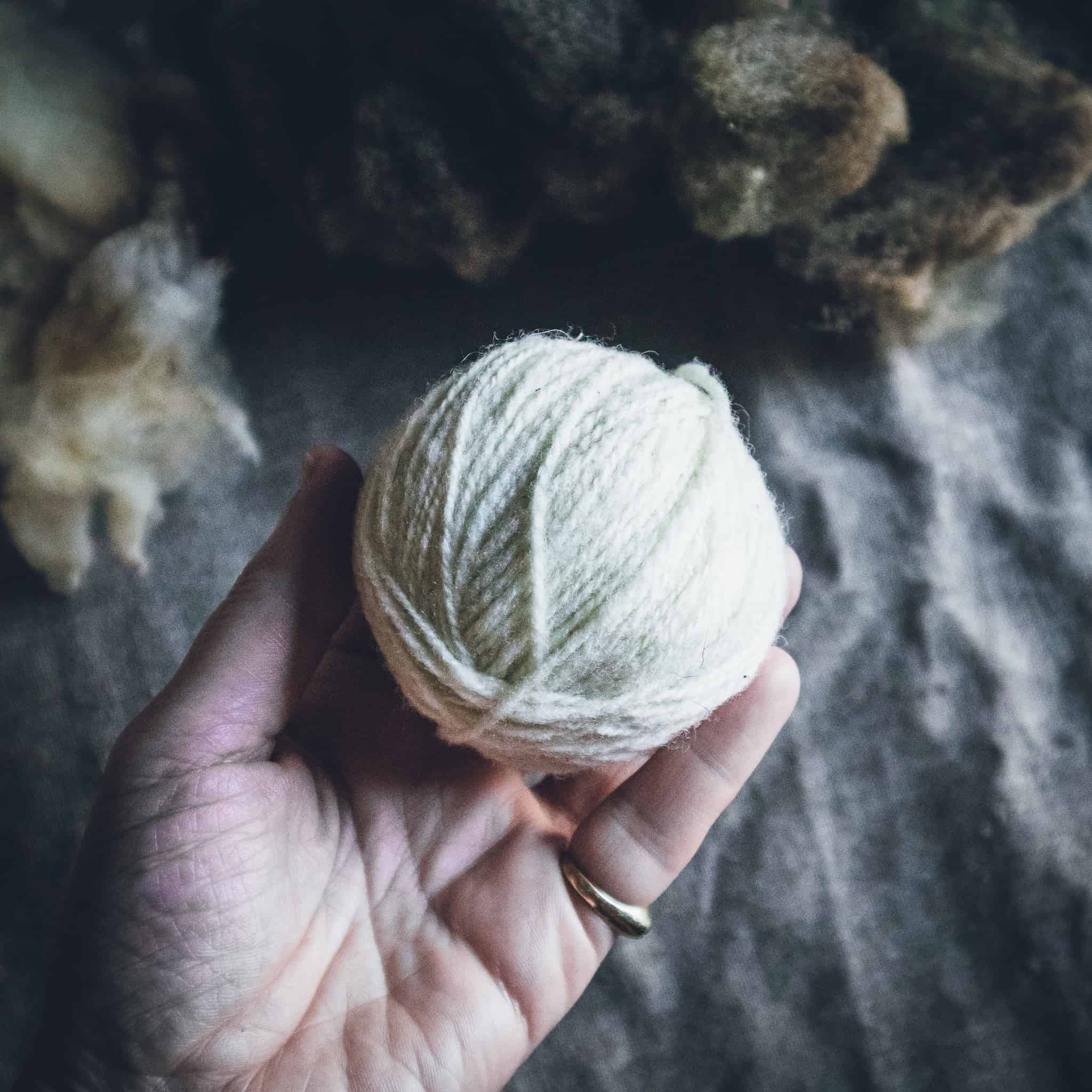 A hand holding a ball of white yarn.