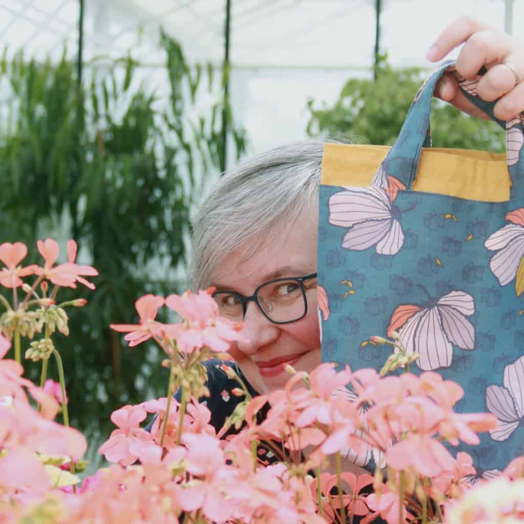 A woman with gray hair peeking out from behind a blue floral bag.