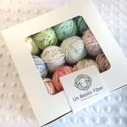 Balls of pastel yarn peer out of a clear-windowed bakery box.