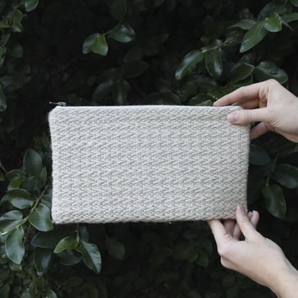 Two hands hold up a white woven clutch.