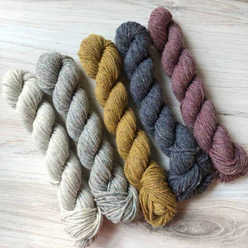 A set of white, gray, gold and pink skeins of yarn.