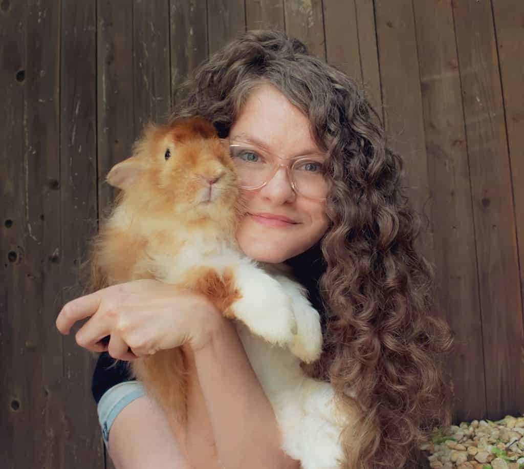 A woman with long curly hair holding a white and gold rabbit.