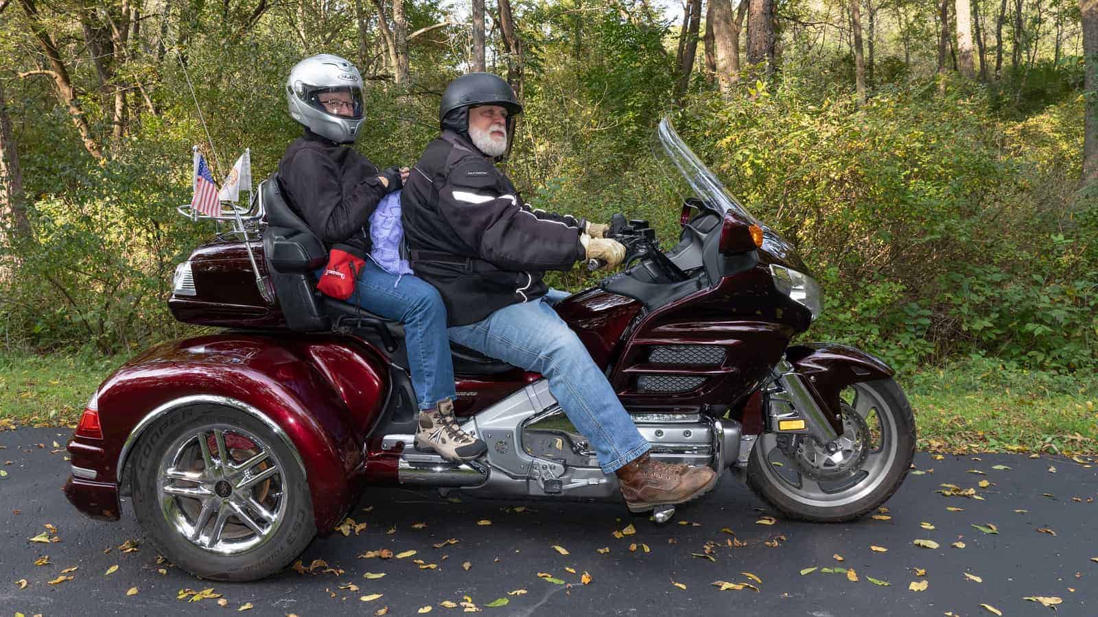 Two people on a motorcycle, the one in the back knitting on a purple project. 