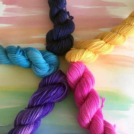 Pink, purple, blue, black and yellow mini skeins in a circle.