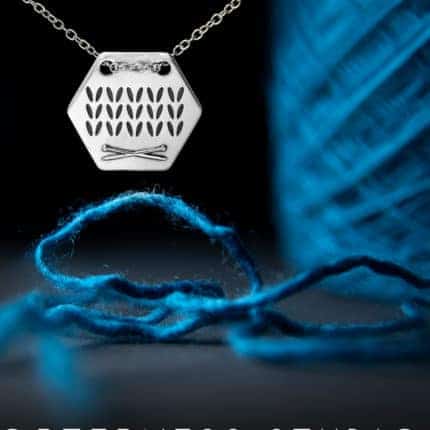 A silver honeycomb necklace with knit stitches next to a cake of blue yarn.