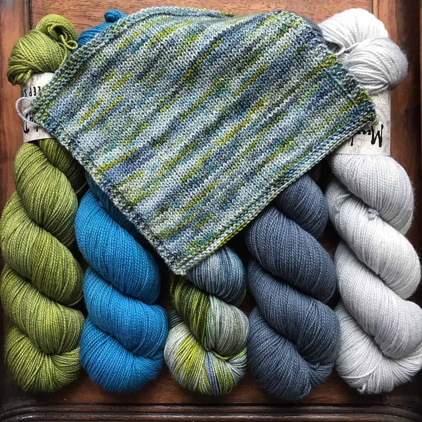 A blue, green and gray knitting swatch over skeins of yarn.