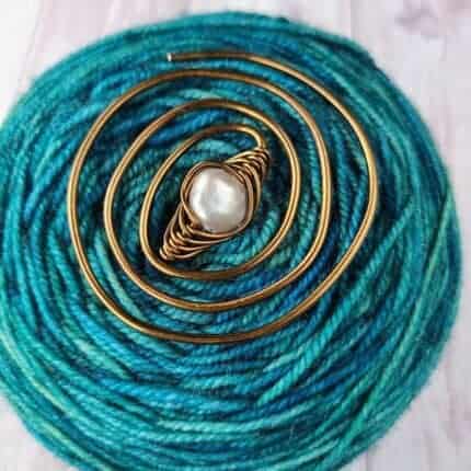 A copper swirl with a pearl on a cake of turquoise yarn.