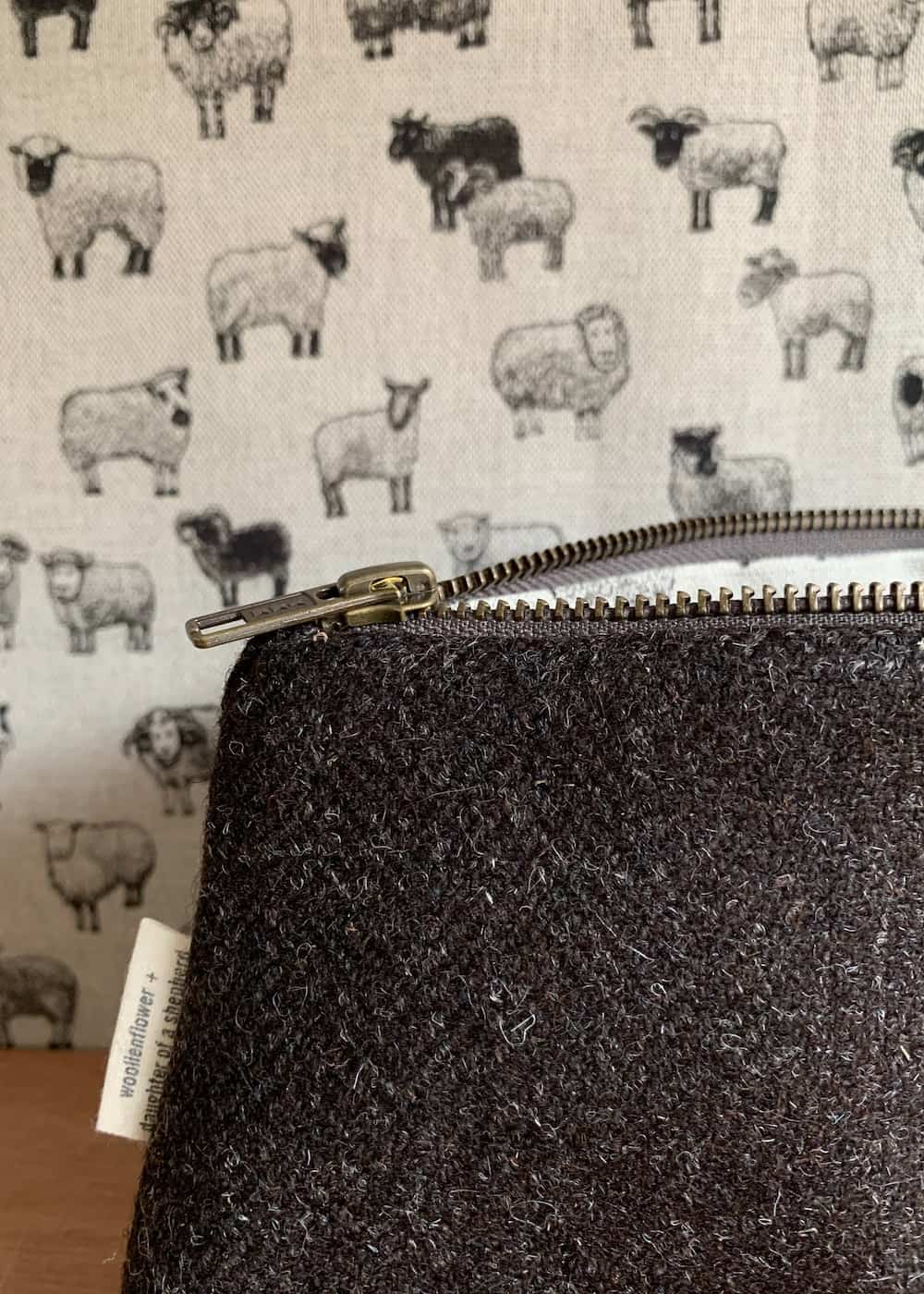 A brown/black tweed pouch in front of fabric with sheep.