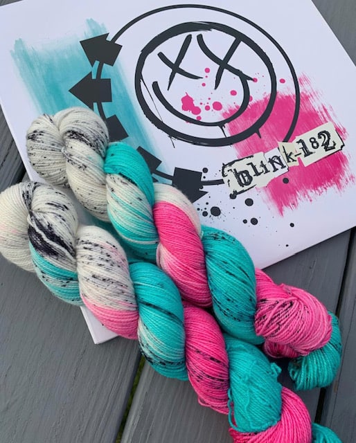 Bright pink, aqua, black and white yarn next to a poster for blink 182.